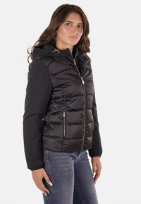 Giubbotto smanicato nero con cappuccio, caratterizzato da sezioni trapuntate, hardware dorato e tasche con zip. Realizzato in materiale leggero e lucido.