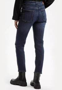 Granatowe dżinsy o przylegającym kroju, z standardowymi kieszeniami z tyłu i wykończonymi nogawkami, w zestawie z czarnymi botkami za kostkę.