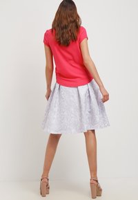 Světle růžový top s krátkými rukávy v kombinaci s texturovanou bílou sukní po kolena s květinovým vzorem a záhyby. Tmavě béžové sandály na vysokém podpatku.