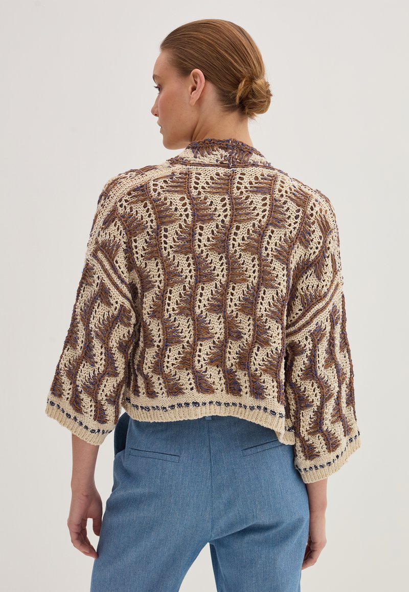 Cardigan in beige a maglia con un motivo a onde, con dettagli blu. Design corto con maniche larghe e trama a rete aperta.