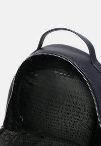 Zaino in pelle blu navy con texture liscia, dotato di chiusura a zip e interno foderato con un motivo a logo "Armani Exchange" che si ripete.