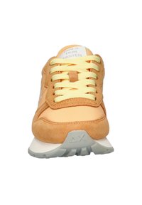 Sneaker arancione in suede e tessuto con lacci gialli, dotata di una suola intermedia bianca e una suola esterna in gomma grigia. Il testo sulla linguetta recita "LE RAGAZZE CORRONO PIÙ VELOCE."