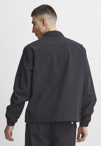 Sort letvægtsjakke med krave, elastiske manchetter og lige kant. Glat tekstur, minimalistisk design og ingen synlige mønstre.