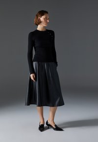 Black ribbed long-sleeve top with side button detail, paired with a flowing black leather midi skirt and glossy black pointed-toe heels.