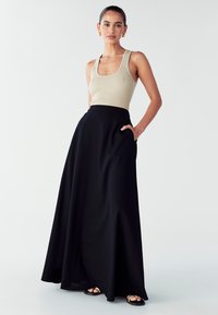 Černá maxi sukně s hladkou texturou, vysokým pasem a bočními kapsami. V kombinaci s těsným béžovým žebrovaným topem. Jednoduchý, elegantní design.