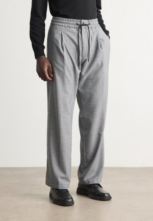 Gray plaid trousers with a relaxed fit, elasticated waistband, pleats, and a drawstring, paired with black shoes.