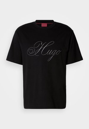T-shirt en coton noir avec un grand logo "Hugo" argenté en écriture cursive sur le devant. Manches courtes et col rond.