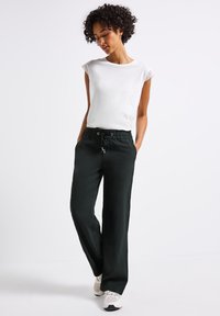 Vit överdel med kort ärm och spetsdetaljer, tillsammans med löst sittande, mörkgröna byxor med elastisk midja och snörning.