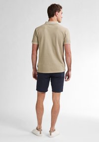 Beige polo tričko s krátkými rukávy, texturovaná látka a límeček, doplněné o námořnické šortky a béžové tenisky. Zobrazeno ze zadní strany.