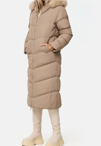 Beżowy puchowy płaszcz z kapturem z sztucznego futra, pionowy pikowany wzór, dwie boczne kieszenie i zamek błyskawiczny, w połączeniu z kremowymi kozakami do kolan.
