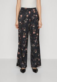 Pantaloni ampi in satin floreale di colore blu navy con fiori multicolori. Caratterizzati da una vita alta e dettagli plissettati, abbinati a scarpe basse nere a punta.