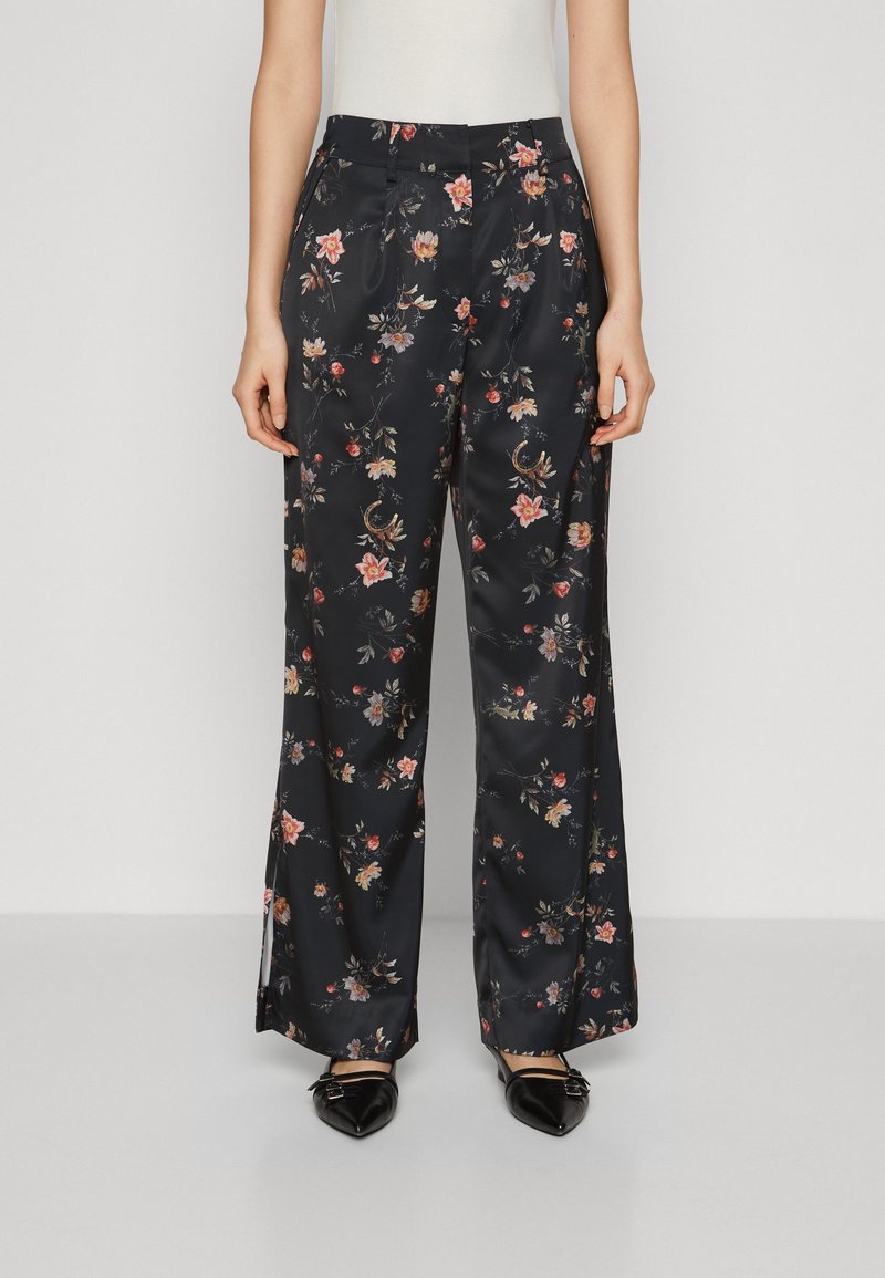 Pantaloni ampi in satin floreale di colore blu navy con fiori multicolori. Caratterizzati da una vita alta e dettagli plissettati, abbinati a scarpe basse nere a punta.