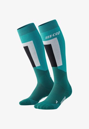 Calze a compressione in teal con accenti neri e grigi. Caratterizzate da motivi geometrici. Realizzate in tessuto traspirante con polsini a coste.