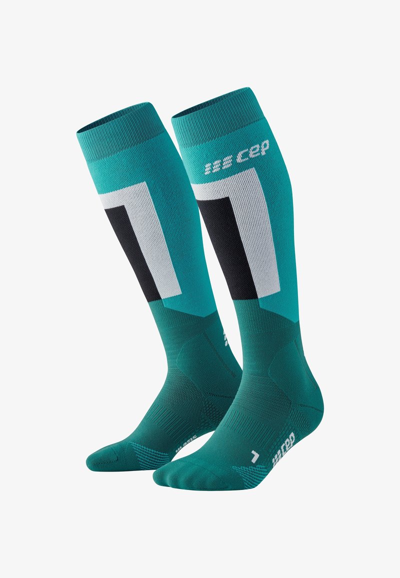 Compressionsokken in teal met zwarte en grijze accenten. Beschikt over geometrische patronen. Gemaakt van ademend materiaal met geribde boorden.