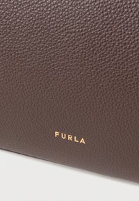 Brązowy portfel ze skóry o fakturze z tłoczonym logo „FURLA” w złotym kolorze, ukazujący delikatny wzór ziarna i prostokątny kształt.
