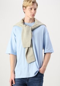 Light blue cotton t-shirt with short sleeves, paired with a knitted beige scarf draped over shoulders. Scarf features ribbed edges.
