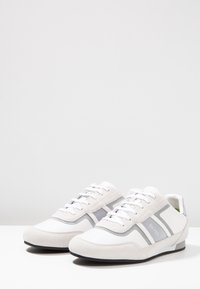 Vita sportskor i en kombination av mocka och mesh-material, med grå detaljer och en strömlinjeformad design. Snörning och gummisula.