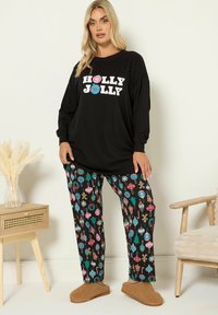 Mustat pitkät hihaiset paidat, joissa on "HOLLY JOLLY" -teksti, yhdistettyinä värikkäisiin kuosisukkiin, joissa on joulukoristeita mustalla taustalla.