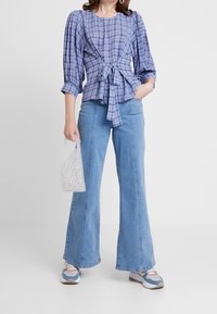 Blå og hvid plaid skjorte med pufærmer og knyttet talje, parret med lyseblå bredde jeans og en lille perlebehandlet håndtaske.