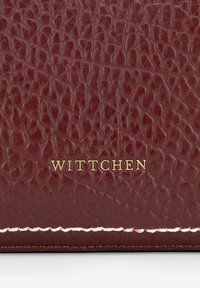 Portafoglio in pelle bordeaux con superficie testurizzata, caratterizzato da una marcatura dorata "WITTCHEN" e orlo bianco.