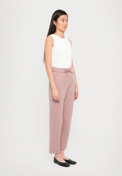White sleeveless top, light pink wide-leg pants with a drawstring waist, and black flat shoes. Smooth fabric with a relaxed fit.