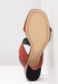 Sandale rouge pour femme avec bout ouvert et talon bloc, vue de la semelle affichant un motif triangulaire décoratif et une base de talon texturée.