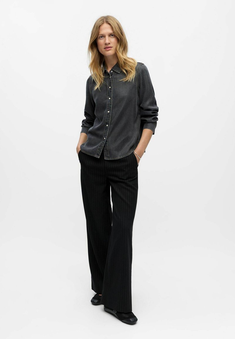 Chemise en denim grise à boutons avec manches longues, associée à un pantalon large à rayures noires et des ballerines noires. Design simple et moderne.
