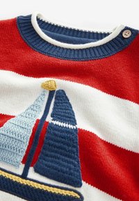 Un pull en laine tricoté rouge et blanc à rayures avec une broderie de voilier bleu et jaune. Il présente un col en côtes bleu marine et un détail de bouton.