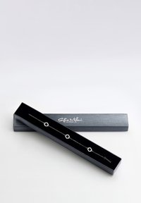 Bracciale d'argento con accenti esagonali, esposto in una scatola nera con finitura liscia e testo del logo in bianco.