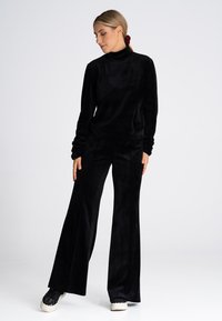 Czarny komplet dresowy z aksamitnego materiału z długimi rękawami i bluzką z wysokim kołnierzem, w zestawieniu z szerokimi spodniami. Posiada miękką teksturę i luźny fason.