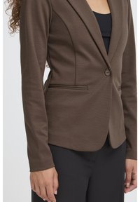 Brun figursydd kavaj med knappstängning, jackslag med hack, och två framfickor, tillverkad av ett texturerat stretchtyg.