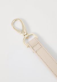 Beige lærrem med teksturert overflate, utstyrt med en gullfarget metallspenne og ring for sikker feste.
