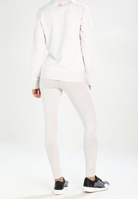 Jasnoszara bluza i pasujące legginsy, oba dopasowane, z teksturowanej tkaniny. Na obuwiu sportowym dominują czarne kolory. Bluza ma małe logo.