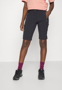 Shorts de sport noirs au design ajusté, dotés de poches zippées et d'un ourlet roulé. Portés avec des chaussures noires et des chaussettes bordeaux.