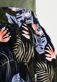 Gonna floreale con una base nera e motivi di foglie colorate in rosa, verde e blu, completata da dettagli con bottoni neri in vita.