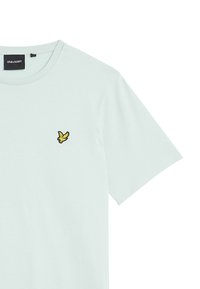 Camiseta de algodón verde menta clara con cuello redondo y mangas cortas, que presenta un pequeño logo bordado en amarillo y negro en el pecho.