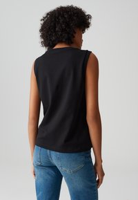 Top senza maniche nero in cotone, con scollatura rotonda e vestibilità comoda, abbinato a jeans in denim blu. Design semplice senza motivi.