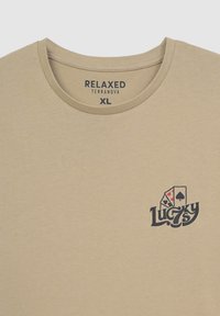 T-shirt di cotone beige con scollatura rotonda, caratterizzato da una stampa grafica di carte da gioco e il testo "Lucky 7s" in nero. Taglia XL.