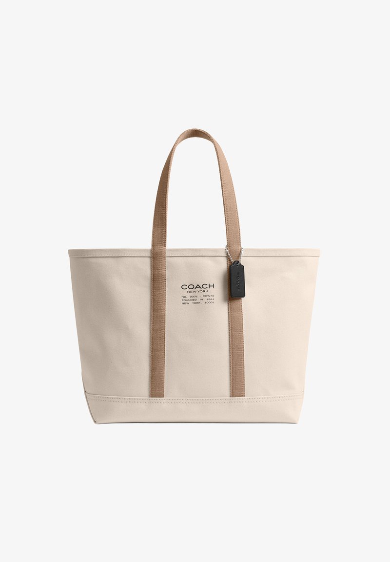 Sac cabas en toile beige avec poignées couleur cuir, étiquette Coach noire et logo Coach New York au centre devant.