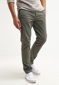 Oliwkowe chinosy o tapered z bawełny, charakteryzujące się casualowym designem, bocznymi kieszeniami oraz elastycznymi mankietami, zestawione z białymi trampkami.