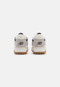 Baskets en daim gris avec accents noirs, col en mesh blanc et semelles en caoutchouc marron. Elles présentent le logo New Balance sur le talon.