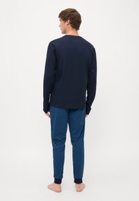Camisola de manga longa azul-marinho combinada com calças de pijama azul estampadas com um design geométrico, cintura elástica e punhos ajustados.