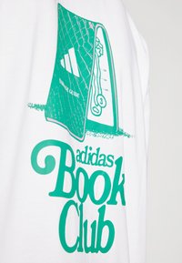 Balta T-krekls ar zaļu grāmatas vāka grafiku, uz kuras redzams teksts "adidas Book Club" un līniju ilustrācijas, radot rotaļīgu dizainu.