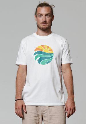 Witte katoenen t-shirt met een ronde afbeelding van een oranje zon en blauw-groene golven, wat een strandthema ontwerp creëert.