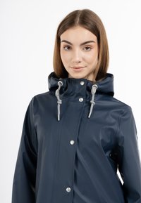 Marinblå vattentät regnjacka med huva, grå dragband, tryckknappar och en glansig yta. Lättviktsmaterial och stilren design.