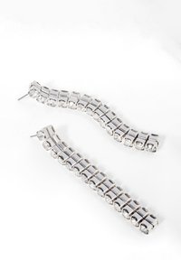 Boucles d'oreilles en argent, de forme courbée, ornées de strass clairs montés sur des maillons carrés, reflétant la lumière avec une texture lisse.
