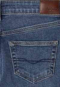 Džinsai su išblukusia tamsiai mėlyna medžiaga, geltonais siūlais ir stačiakampiu rudos odos žyme, išspausdintu "Pepe Jeans London".