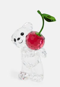 Kristallfigur av en björn som håller en röd, fasetterad körsbär med ett grönt blad. Klar, slät yta med detaljerade drag.