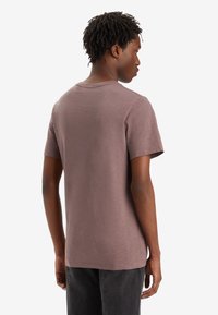 Kurzärmliges T-Shirt mit Rundhalsausschnitt in gedämpfter Mauve-Farbe, aus weichem Stoff mit leicht strukturierter Oberfläche, minimalistischen Nähten und lässigem Schnitt.