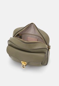 Borsa a mano in pelle verde oliva con superficie testurizzata, hardware dorato, chiusura con zip e un ampio interno con fodera rosa e etichetta.
